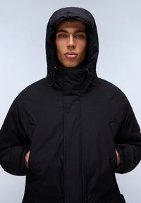 Zwarte hoodie jas met een hoge kraag, ritssluiting aan de voorkant, verstelbare trekkoorden op de capuchon en zijzakken. Soepele, matte textuur.