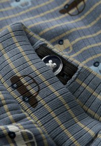 Niebieska tkanina w paski z małymi motywami samochodów w brązowym i jasnoniebieskim kolorze. Zbliżenie na guzik na koszuli.