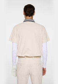 Beige kortärmad polo med en krage i svart och vitt randigt mönster, i kombination med ljusbeiga byxor och ett flätat bälte. Vit långärmad undertröja synlig.