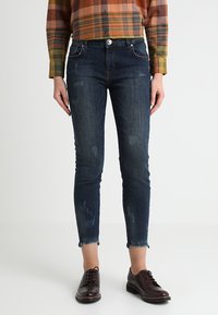 Mörkblå denim skinny jeans med slitna detaljer och fransade fållar, tillsammans med en rutig skjorta och mörka snörskor.
