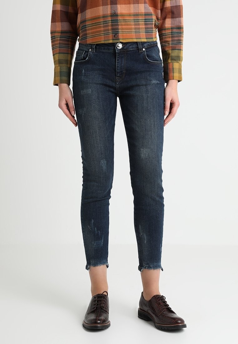 Mörkblå denim skinny jeans med slitna detaljer och fransade fållar, tillsammans med en rutig skjorta och mörka snörskor.