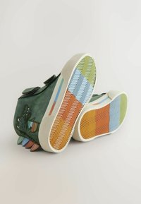 Zöld sportcipő texturált bőrhatással, tépőzáras pántokkal, játékos krokodilmintával és többszínű, mintás gumitalppal.