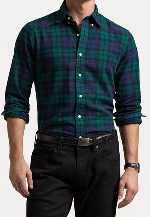 Groen en marineblauwe geruite overhemd met kraag, lange mouwen en witte knopen, gecombineerd met zwarte broek en een zwarte riem.