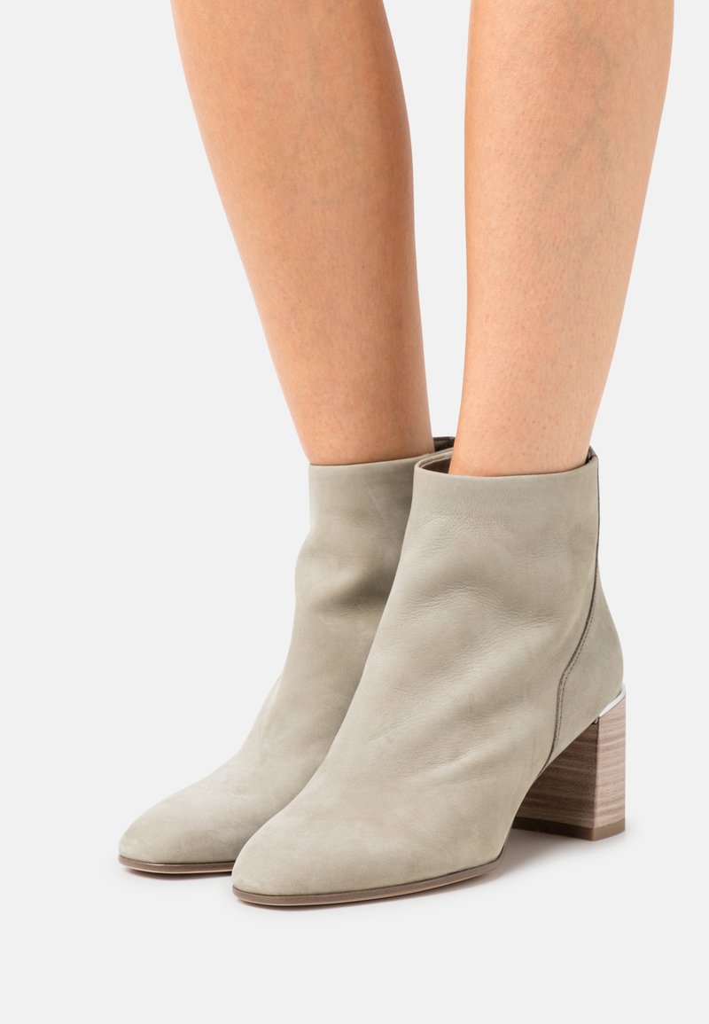 Femme portant des bottines en daim gris clair avec talons blocs en bois sur un fond uni.