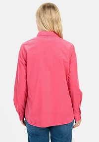 Langdurige overhemd in een levendige roze kleur met een button-down kraag. Heeft een gladde textuur en een licht gebogen zoom. Achteraanzicht weergegeven.
