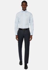 Chemise habillée à manches longues bleu clair avec col boutonné, assortie à un pantalon noir marine et des chaussures de ville noires. Tissu lisse, coupe ajustée.