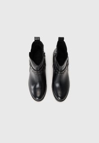 Black leather ankle boots with a smooth finish, circular cut-out accents, side zippers, and textured heel detail.