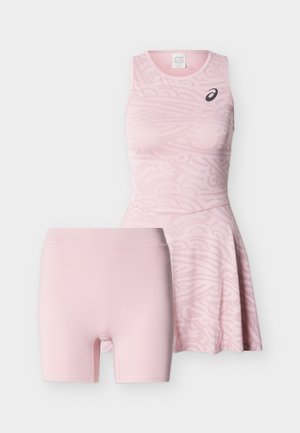 Robe de sport rose clair sans manches avec un motif subtil et un logo noir, assortie à un short moulant rose clair uni.