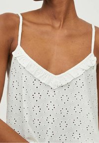 Camisola bianca in cotone con scollatura a V e spalline sottili. Presenta un motivo ricamato ad occhiello e un dettaglio di scollatura a volant. Tessuto leggero.