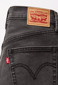 Μαύρα τζιν από τζιν ύφασμα με ταμπέλα από ταμπά δέρμα με κόκκινα γράμματα και κόκκινη ετικέτα στην τσέπη που φέρει το λογότυπο της Levi's.