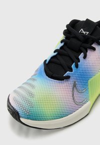 Gros plan sur une chaussure de sport colorée avec une tige en mesh, des lacets noirs et un logo argenté distinctif sur le côté près des orteils.