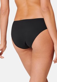 Bas de bikini noir en tissu lisse. Présente une jambe haute avec une couverture minimale et un design sans coutures. Pas de matériel ou de motifs visibles.