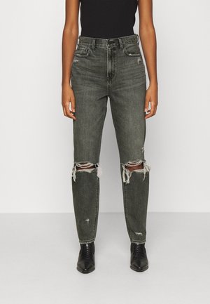 Persoon draagt hooggeplaatste, vervaagde zwarte ripped jeans met rafelige knieën, gecombineerd met zwarte puntige enkellaarsjes en een zwart topje.