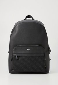 Svart ryggsäck med slät yta, strukturerad form, framficka med dragkedja och diskret logotypdetalj. Tillverkad av hållbara material med ett texturerat mönster.