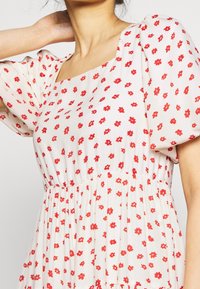 Bílé šaty s červeným květinovým potiskem, čtveratý výstřih, krátké nabírané rukávy, nabíraný pas a lehký materiál.