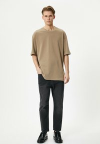 Camiseta oversized beige de manga corta, combinada con jeans de mezclilla oscura y zapatos negros. Diseño minimalista con un ajuste relajado y textura suave.