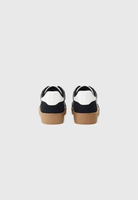 Zwarte suede en leren sneakers met een witte hielaccent en een bruine rubberen zool. Kenmerkt zich door een gladde textuur en een afgeronde vorm.
