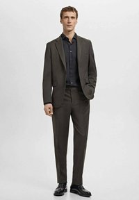 Donkergrijs pak met een enkele rij knopen en bijpassende broek, gecombineerd met een zwart overhemd en zwarte schoenen. Gladde textuur, op maat gemaakt.