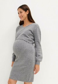 Robe pull en tricot grise avec un décolleté en V et des manches longues, dotée d'une silhouette ajustée qui s'adapte à un ventre en croissance. Texture douce.