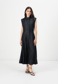 Mørk denim, ermeløs kjole med knappestolpe, utsvingt skjørt og sidelommer. Avslutningene inkluderer pent søm og en tettsittende midje.