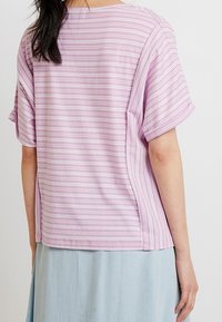 Lila randig topp med korta ärmar och avslappnad passform, med horisontella vita ränder och en mjuk tygkänsla.