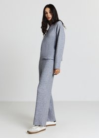 Completo comodo grigio in maglia composto da una maglia a taglio rilassato con orlo dritto e pantaloni a gamba larga, abbinato a sneakers bianche.