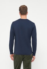 Hosszú ujjú, sötétkék pamut póló kerek nyakkal és sima textúrával, olívazöld kordbársony nadrággal párosítva.