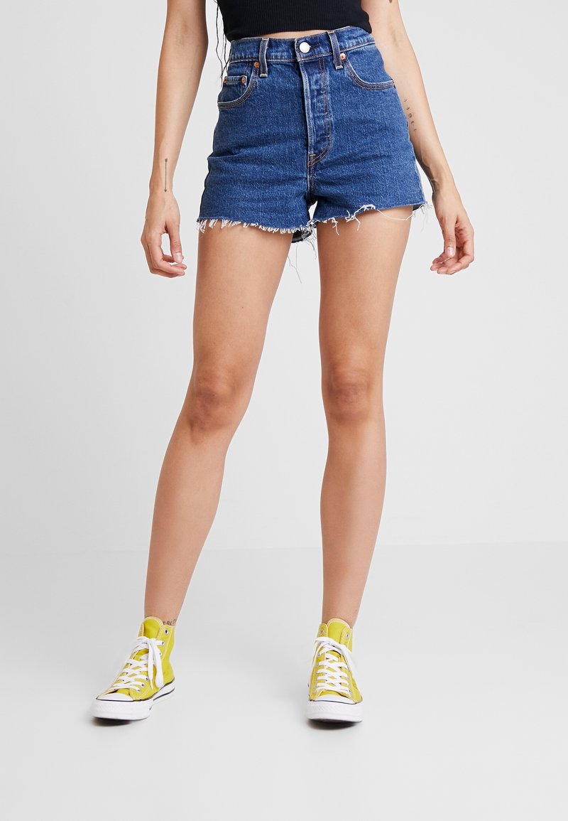 Höga blå denimshorts med fransad fåll, fem fickor och kontrasterande sömmar. Kombinerade med gula högskor.