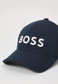 Sötétkék sapka textúrált anyagból, ívelt karimával és fehér hímzett "BOSS" felirattal az elülső panelen. Klasszikus dizájn.