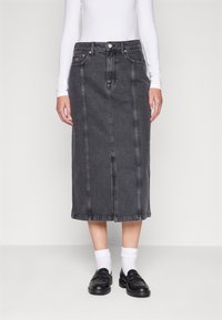 Svart denim midi-kjol med framsömmar, figursydd midja och två sidofickor, tillsammans med en vit långärmad topp och svarta loafers.