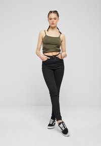 Czarne jeansy z wysokim stanem i dopasowanym krojem, zestawione z dopasowanym oliwkowozielonym topem na ramiączkach. Z detalem w postaci wiązania na dole. Czarne trampki.