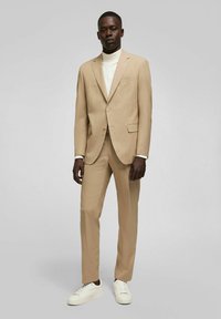 Beige, op maat gemaakt colbert met subtiele streepjes, met geknipte revers en zijzakken, gecombineerd met een witte coltrui en witte sneakers.