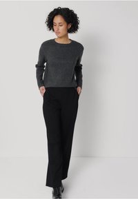 Šedý pletený svetr s kulatým výstřihem, spárovaný s černými elegantními kalhotami se bočními kapsami. Hladké textury, minimalistický design.