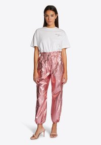 Weißes T-Shirt mit kurzen Ärmeln und dem Text "California"; pinke metallische Hose mit elastischen Bündchen und Gummizugbund; beige Absatzsandalen.