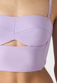 Lavender cropped top with a structured bust and cut-out detail. Made from smooth fabric, featuring thin adjustable straps and seam accents.