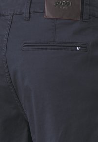 Pantaloni blu navy con una texture liscia, caratterizzati da una piccola tasca posteriore con cucitura orizzontale e un'etichetta in pelle impresso con "JOOP! JEANS".