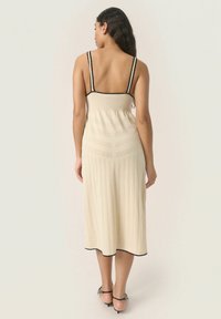 Abito in maglia color crema con strisce verticali, corpino a coste e dettagli in nero. Design di lunghezza media con una vestibilità rilassata.