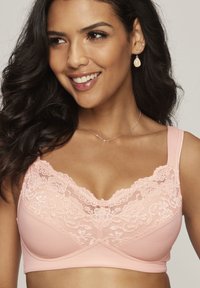 Light pink bra with lace trim at the neckline, soft fabric cups, wide straps, and subtle floral pattern on lace detailing.