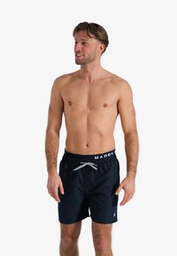 Marineblauwe zwemshorts met een elastische tailleband, trekkoord en witte "HAPPY" tekst. Gemaakt van een gladde, lichte stof.
