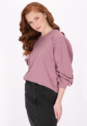 Helllila Pullover mit Puffärmeln und gerippten Bündchen, kombiniert mit einem hochgeschnittenen schwarzen Jeansrock. Glattes Material und lässige Passform.