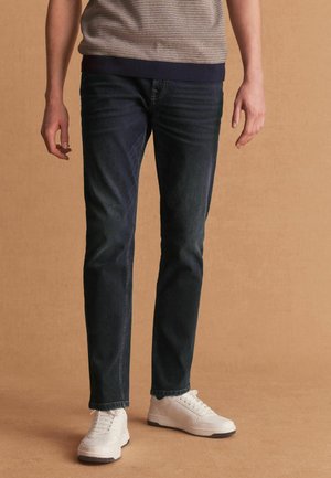 Jeans negre închis cu croială dreaptă și o textură subtilă, asortați cu adidași albi cu un finisaj din piele lucioasă.