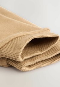 Paita rukou beige yang dilipat dengan tekstur wol halus yang terlihat di permukaan yang terang.