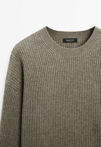 Grijze gebreide trui met een geribbelde textuur, ronde hals en doorhangende schouders. Label zegt "Massimo Dutti." Zacht, casual ontwerp.