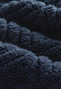 Granatowy, pluszowy materiał o miękkiej, teksturowanej powierzchni, z głębokimi, puszystymi włóknami w falistym wzorze. Idealny dla ciepła i komfortu.