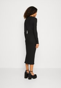 Robe noire moulante en rib, à manches longues, longueur mi-mollet, col rond et légèrement évasée à l'ourlet, associée à des chaussures à plateforme noires et chunky.