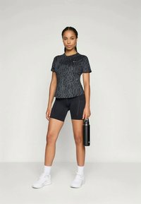 Black patterned athletic t-shirt with short sleeves and black cycling shorts, paired with white sneakers and holding a black water bottle.