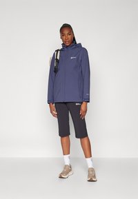 Marineblauwe waterdichte jas met een capuchon, rits aan de voorkant en logo-detail. Gecombineerd met donkere shorts en sneakers in neutrale tinten. Eenvoudig ontwerp.