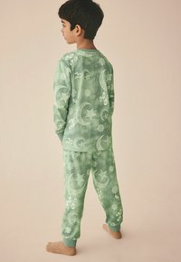 Grünes Pyjama-Set mit weißen Halbmonden, Sternen und Laternen. Weicher Stoff mit einem Batik-Effekt. Gerippte Bündchen an den Ärmeln und Hosen.