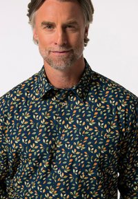 Námornická košile s knoflíky, zdobená listovým vzorem v zelené, oranžové a krémové barvě. Vyrobena z lehké látky s hladkou strukturou.