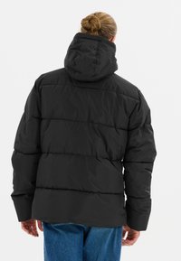 Doudoune noire avec capuche, présentant un design matelassé, une surface texturée et une coupe décontractée, associée à un jean en denim bleu.